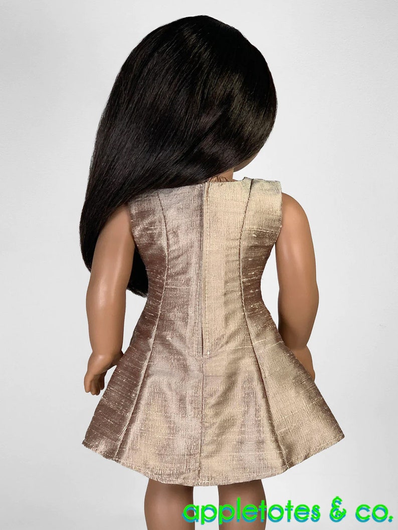 May include: A sleeveless dress for a doll, made of a shimmery gold fabric. The dress has a fitted bodice and a flared skirt.