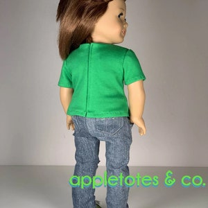 K&ouml;nnte beinhalten: Eine Puppe tr&auml;gt ein gr&uuml;nes T-Shirt mit kurzen &Auml;rmeln und eine blaue Jeans mit Used-Look. Die Puppe tr&auml;gt schwarze Sneaker mit gr&uuml;nen Akzenten. Die Puppe hat braunes Haar und schaut &uuml;ber die Schulter.