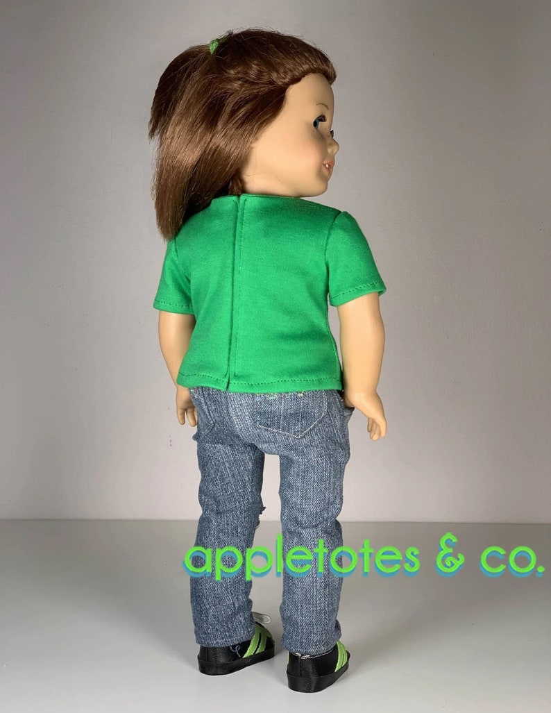 K&ouml;nnte beinhalten: Eine Puppe tr&auml;gt ein gr&uuml;nes T-Shirt mit kurzen &Auml;rmeln und eine blaue Jeans mit Used-Look. Die Puppe tr&auml;gt schwarze Sneaker mit gr&uuml;nen Akzenten. Die Puppe hat braunes Haar und schaut &uuml;ber die Schulter.