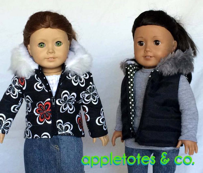 May include: Two dolls wearing winter outerwear. The doll on the left is wearing a black and white puffer jacket with a white faux fur hood. The doll on the right is wearing a black puffer vest with a gray faux fur hood and a gray and white polka dot lining.