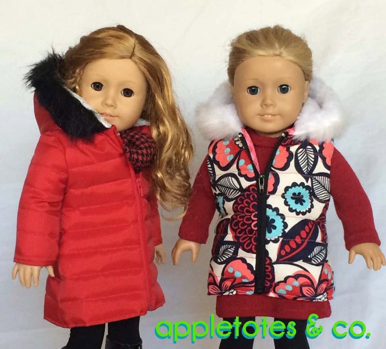May include: Two dolls wearing winter clothing. The doll on the left is wearing a red puffer jacket with a black fur hood. The doll on the right is wearing a cream-colored vest with a floral print and a white fur hood. Both dolls are wearing red shirts and black pants.