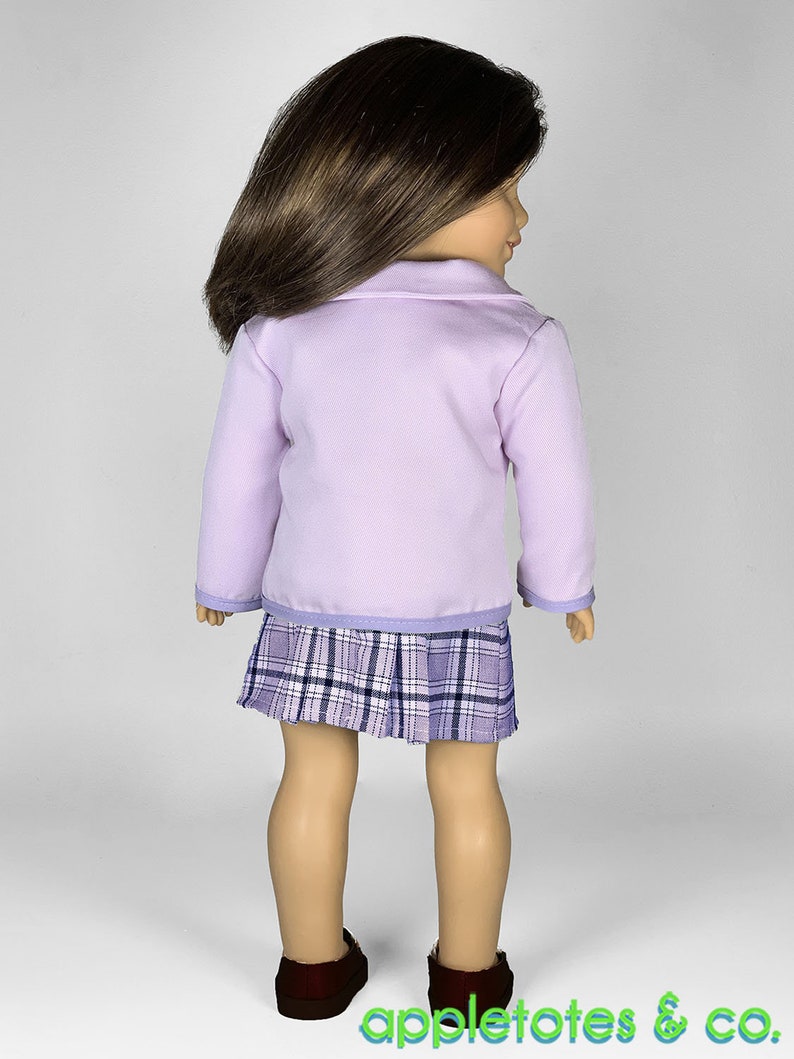 May include: A lavender blazer with long sleeves and a plaid skirt. The doll is wearing brown shoes.