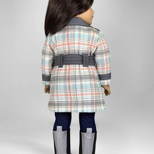 Puede incluir: Una mu&ntilde;eca con un abrigo de cuadros con un cintur&oacute;n gris, leggings azules y botas grises.