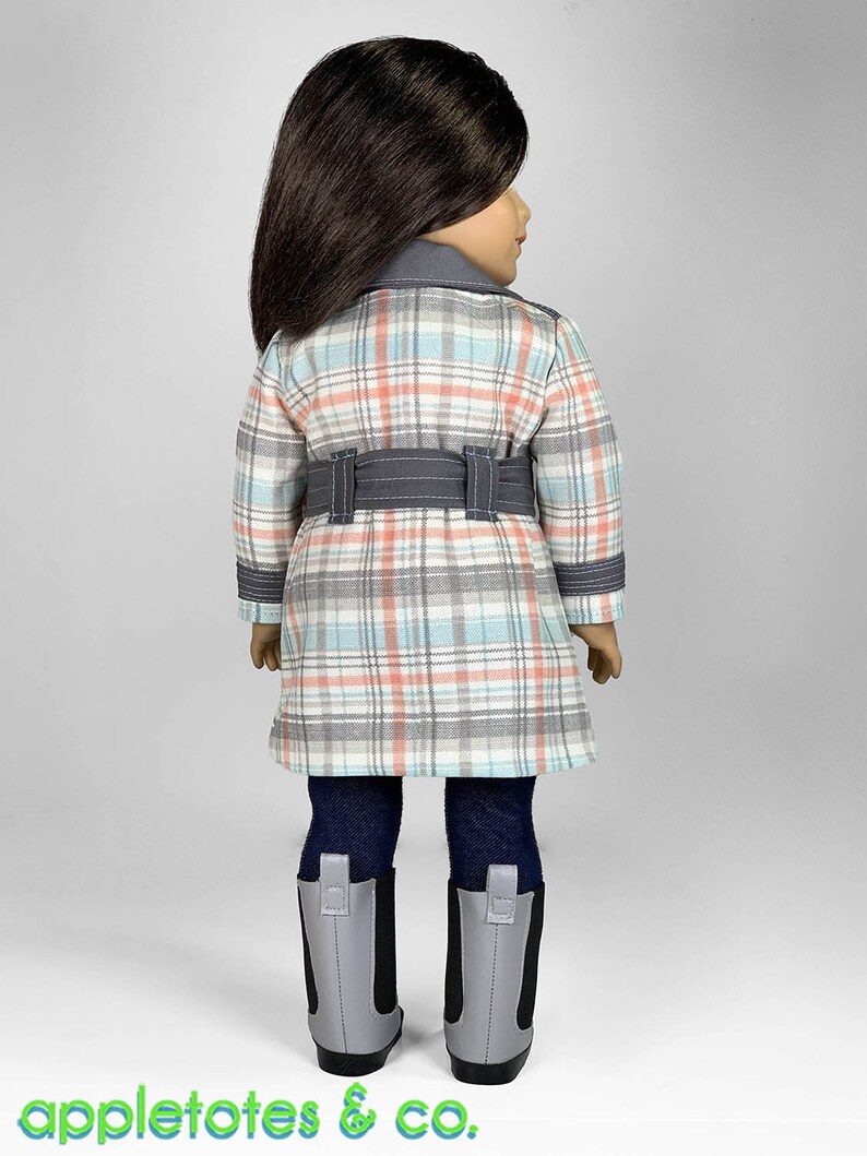 Puede incluir: Una mu&ntilde;eca con un abrigo de cuadros con un cintur&oacute;n gris, leggings azules y botas grises.