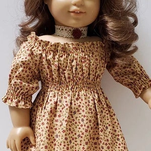 May include: A doll wearing a brown and white floral off-the-shoulder dress with a white lace trim. The dress has a gathered waist and 3/4 sleeves. The doll is wearing a white lace choker with a red flower accent. The doll has long brown hair.