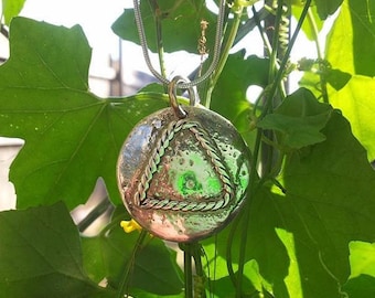 May include: A silver pendant necklace with a round, textured disc featuring a green triangle outlined with a braided rope design.