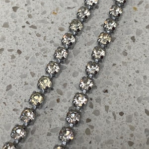 May include: A silver chain with clear rhinestones. The chain is made of small, round rhinestones that are connected by silver links.