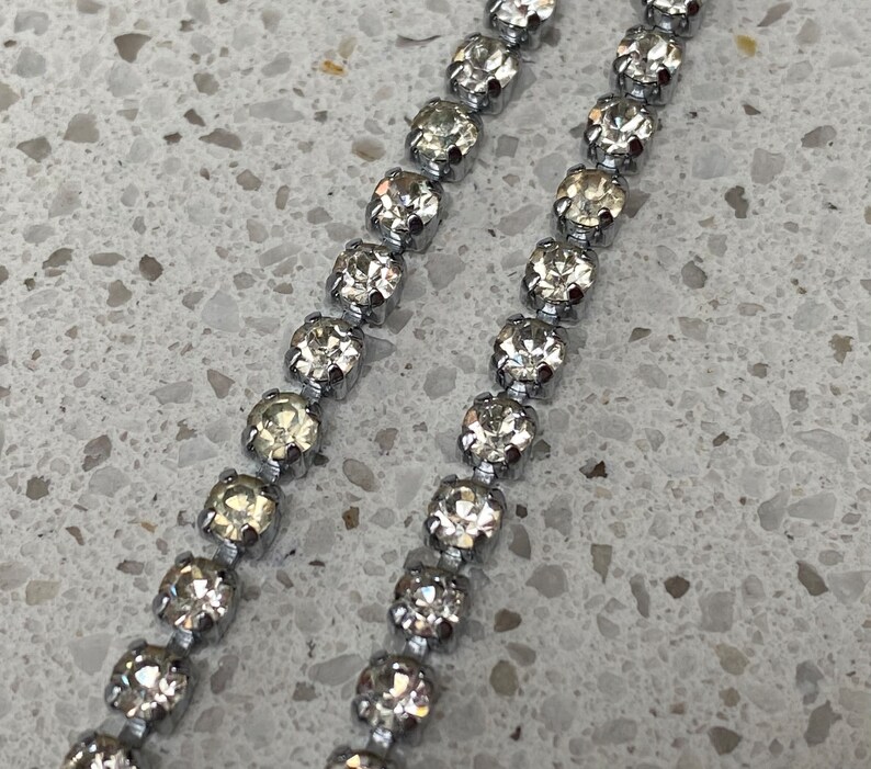 May include: A silver chain with clear rhinestones. The chain is made of small, round rhinestones that are connected by silver links.