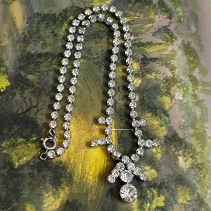 May include: A silver necklace with a large, clear rhinestone pendant. The necklace is made of a chain of small, clear rhinestones.