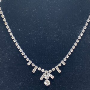 May include: A silver necklace with a delicate chain and a teardrop-shaped pendant adorned with clear rhinestones.