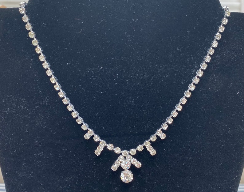 May include: A silver necklace with a delicate chain and a teardrop-shaped pendant adorned with clear rhinestones.
