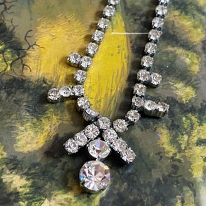 May include: A silver rhinestone necklace with a large, round, faceted rhinestone pendant. The necklace has a delicate, feminine design and is perfect for a special occasion.