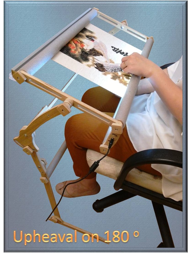Puede incluir: Un soporte de bordado de madera con una tela de color claro estirada sobre &eacute;l. El soporte est&aacute; unido a una silla y tiene un cable enchufado. El texto "Upheaval on 180&deg;" es visible en la parte inferior de la imagen.