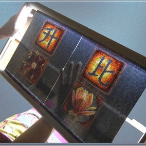 Puede incluir: Primer plano de un aro de bordado negro con una tela azul estirada sobre &eacute;l. La tela tiene un dise&ntilde;o floral y los caracteres chinos "北" y "芽" bordados sobre ella.