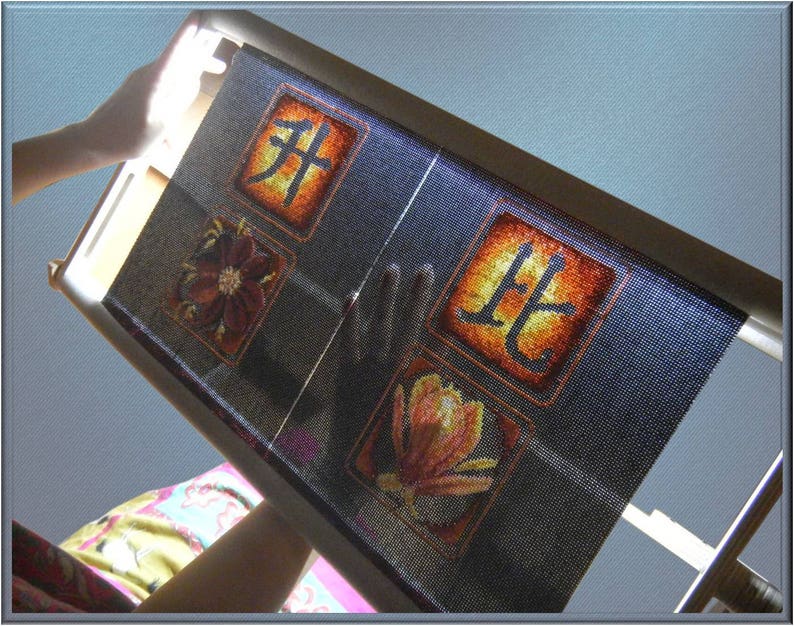 Puede incluir: Primer plano de un aro de bordado negro con una tela azul estirada sobre &eacute;l. La tela tiene un dise&ntilde;o floral y los caracteres chinos "北" y "芽" bordados sobre ella.