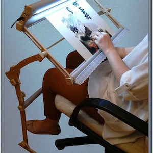 Puede incluir: Un bastidor de madera para bordar con luz incorporada, una persona est&aacute; sentada en una silla y utiliza el bastidor para trabajar en un proyecto de bordado. El proyecto de bordado es una imagen de un p&aacute;jaro.