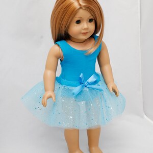 K&ouml;nnte beinhalten: Eine Puppe tr&auml;gt einen blauen Trikot mit einem hellblauen T&uuml;llrock mit silbernem Glitzer. Die Puppe hat langes, glattes, rotbraunes Haar.