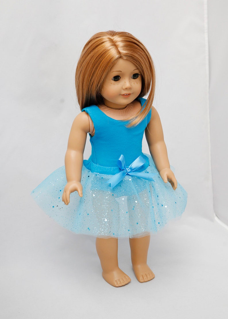 K&ouml;nnte beinhalten: Eine Puppe tr&auml;gt einen blauen Trikot mit einem hellblauen T&uuml;llrock mit silbernem Glitzer. Die Puppe hat langes, glattes, rotbraunes Haar.