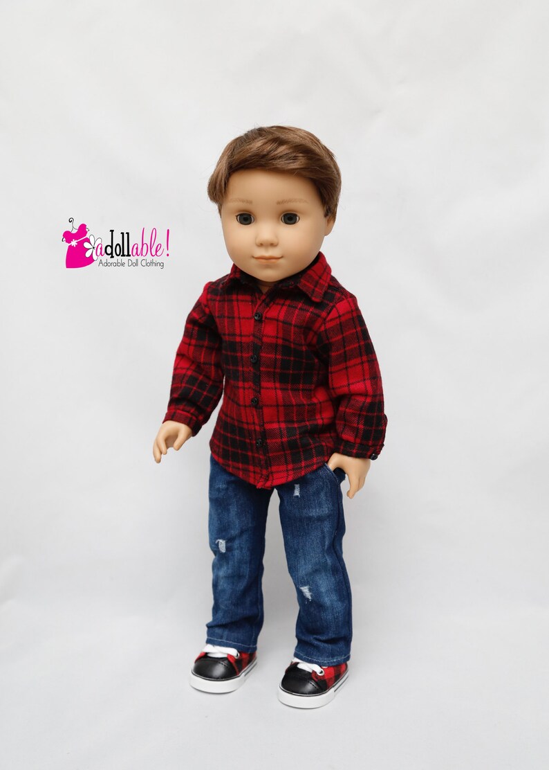 May include: A doll wearing a red and black plaid shirt, blue jeans with distressed details, and black and red sneakers. The doll has brown hair and blue eyes.