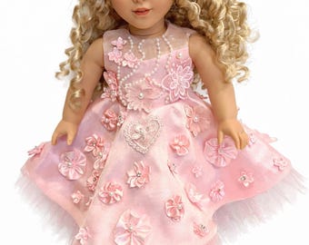 Puede incluir: Muñeca rubia de pelo rizado y ojos azules, vestida con un vestido rosa adornado con flores y perlas. El vestido tiene una falda de tul y un detalle en forma de corazón en el corpiño. Un juguete clásico.