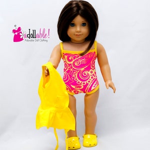May include: A doll wearing a pink and yellow swimsuit with a paisley pattern. The doll is holding a yellow dress and is wearing yellow shoes.