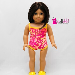 May include: A doll wearing a pink and yellow swimsuit with a paisley pattern. The doll is wearing yellow clogs.