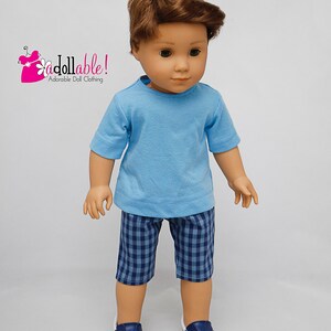 May include: A doll wearing a light blue t-shirt and blue and white checkered shorts. The doll is wearing blue sneakers. The doll has brown hair and blue eyes. The doll is wearing an outfit from "Addollable! Adorable Doll Clothing."