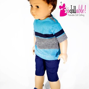 K&ouml;nnte beinhalten: Eine Puppe tr&auml;gt ein blau-wei&szlig; gestreiftes, kurz&auml;rmeliges Hemd, eine dunkelblaue Shorts und blaue Turnschuhe. Die Puppe hat braunes Haar und steht auf einem wei&szlig;en Hintergrund.