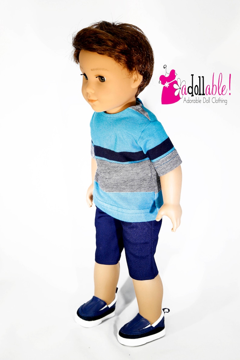 K&ouml;nnte beinhalten: Eine Puppe tr&auml;gt ein blau-wei&szlig; gestreiftes, kurz&auml;rmeliges Hemd, eine dunkelblaue Shorts und blaue Turnschuhe. Die Puppe hat braunes Haar und steht auf einem wei&szlig;en Hintergrund.