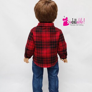 May include: A doll wearing a red and black plaid shirt and blue jeans. The doll has brown hair and is standing on a white background.