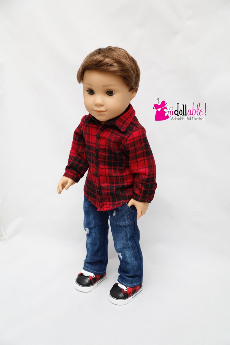 May include: A doll wearing a red and black plaid shirt, blue jeans, and black and red plaid sneakers. The doll has brown hair and blue eyes.