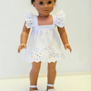 May include: A white doll with brown hair and brown eyes wearing a white eyelet dress and white shoes.