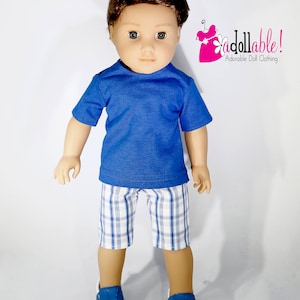 May include: A doll wearing a blue short-sleeved shirt, plaid shorts, and blue sneakers. The doll has brown hair and blue eyes. The image includes the text "addollable! Adorable Doll Clothing".