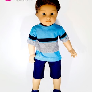 K&ouml;nnte beinhalten: Eine Puppe tr&auml;gt ein blau-graues, gestreiftes T-Shirt mit kurzen &Auml;rmeln, eine dunkelblaue Shorts und dunkelblaue Turnschuhe. Die Puppe hat braunes Haar und braune Augen.