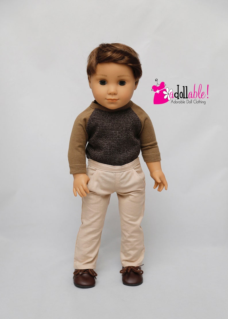 May include: A doll wearing a brown and grey waffle knit shirt with brown long sleeves and beige trousers. The doll is wearing brown shoes. The doll has brown hair and blue eyes. The image includes the text "addollable! Adorable Doll Clothing".