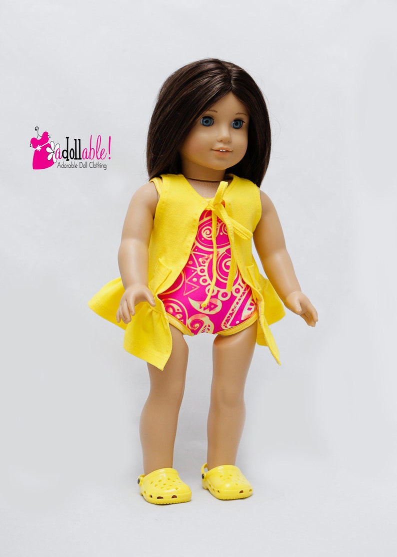 May include: A doll wearing a yellow sleeveless vest over a pink and gold patterned swimsuit. The doll is wearing yellow clogs. The image includes the text "Addollable! Adorable Doll Clothing."
