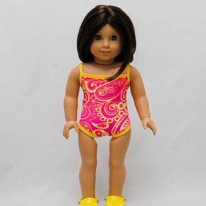 May include: A doll wearing a pink and yellow swimsuit with a paisley pattern. The doll is wearing yellow shoes.