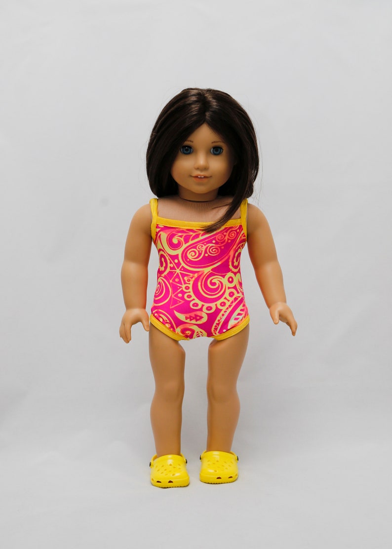 May include: A doll wearing a pink and yellow swimsuit with a paisley pattern. The doll is wearing yellow shoes.