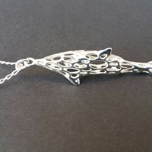 May include: A silver chain necklace with a delicate, openwork dolphin pendant. The dolphin is made of a fine, intricate mesh design.