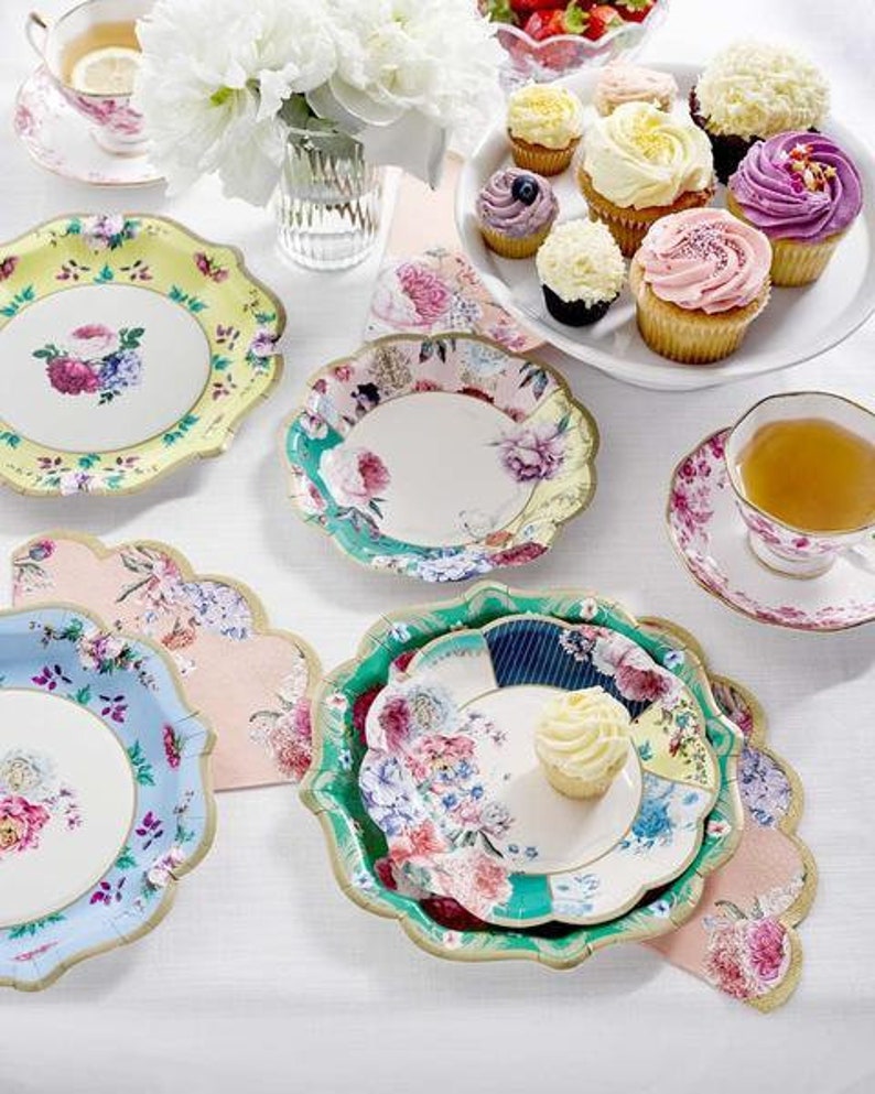 May include: A set of floral patterned paper plates with scalloped edges. The plates are in various colors, including blue, green, pink, and white. There are also cupcakes with colorful frosting on a white table.