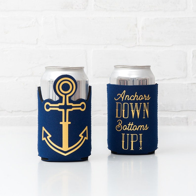 May include: Two navy blue can coolers with gold designs. One features a gold anchor, the other reads "Anchors DOWN Bottoms UP!" in gold lettering. The coolers are designed to hold standard-sized beverage cans.