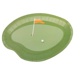 May include: A green paper plate shaped like a golf course. The plate features a golf hole with a white golf ball, a white flag pole, and an orange flag. The plate has a ridged border.