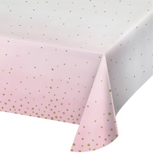 May include: A pink and white tablecloth with a gold polka dot pattern. The tablecloth has a gradient effect, transitioning from white to pink. The gold dots are scattered across the surface, creating a festive look. The tablecloth is folded over, showing the edge.