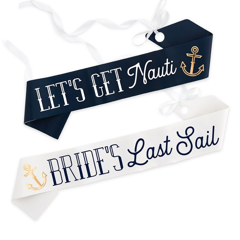 May include: Two nautical-themed sashes. One is navy blue with the text "LET'S GET Nauti" and a gold anchor. The other is white with "BRIDE'S Last Sail" and a gold anchor. Both have white ribbon ties.