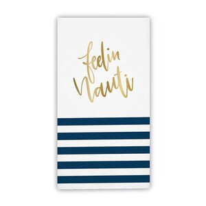 May include: White paper napkin with gold script text "feelin Nauti" above navy blue horizontal stripes. The napkin is rectangular and has a nautical theme.