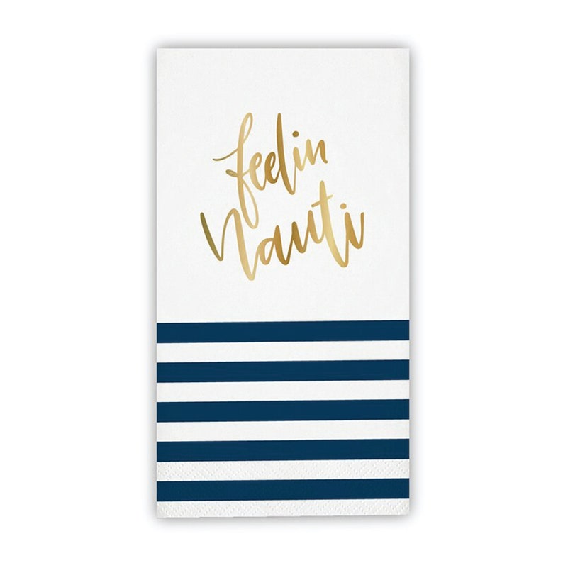 May include: White paper napkin with gold script text "feelin Nauti" above navy blue horizontal stripes. The napkin is rectangular and has a nautical theme.