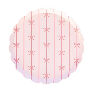May include: A round, scalloped-edge paper plate with a pink and white striped pattern. The plate features evenly spaced pink bows along the vertical stripes, creating a charming and delicate design. Perfect for a baby shower or a birthday party.