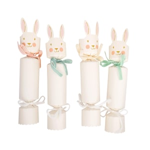 May include: Four white paper crackers with bunny faces and pastel bows. Each cracker has a cylindrical body and a bunny head with pink ears. The bows are in shades of pink, green, and cream. White ribbons secure the ends.