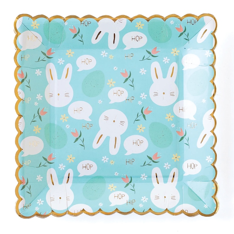 May include: Square blue paper plates with a gold scalloped edge. The plates feature a repeating pattern of white bunnies, flowers, and the words "HOP" and "HIP" in gold.