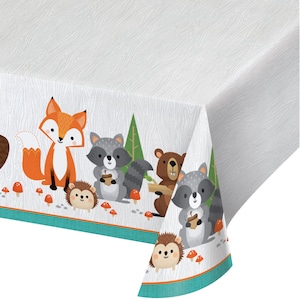 May include: White rectangular tablecloth with a woodland animal border. The border features a fox, raccoons, a bear, and a hedgehog, along with mushrooms and trees. The tablecloth has a wood grain pattern.